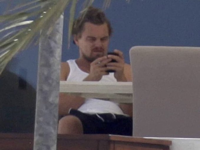 A man sits outside with a laptop open, still staring at his phone.
